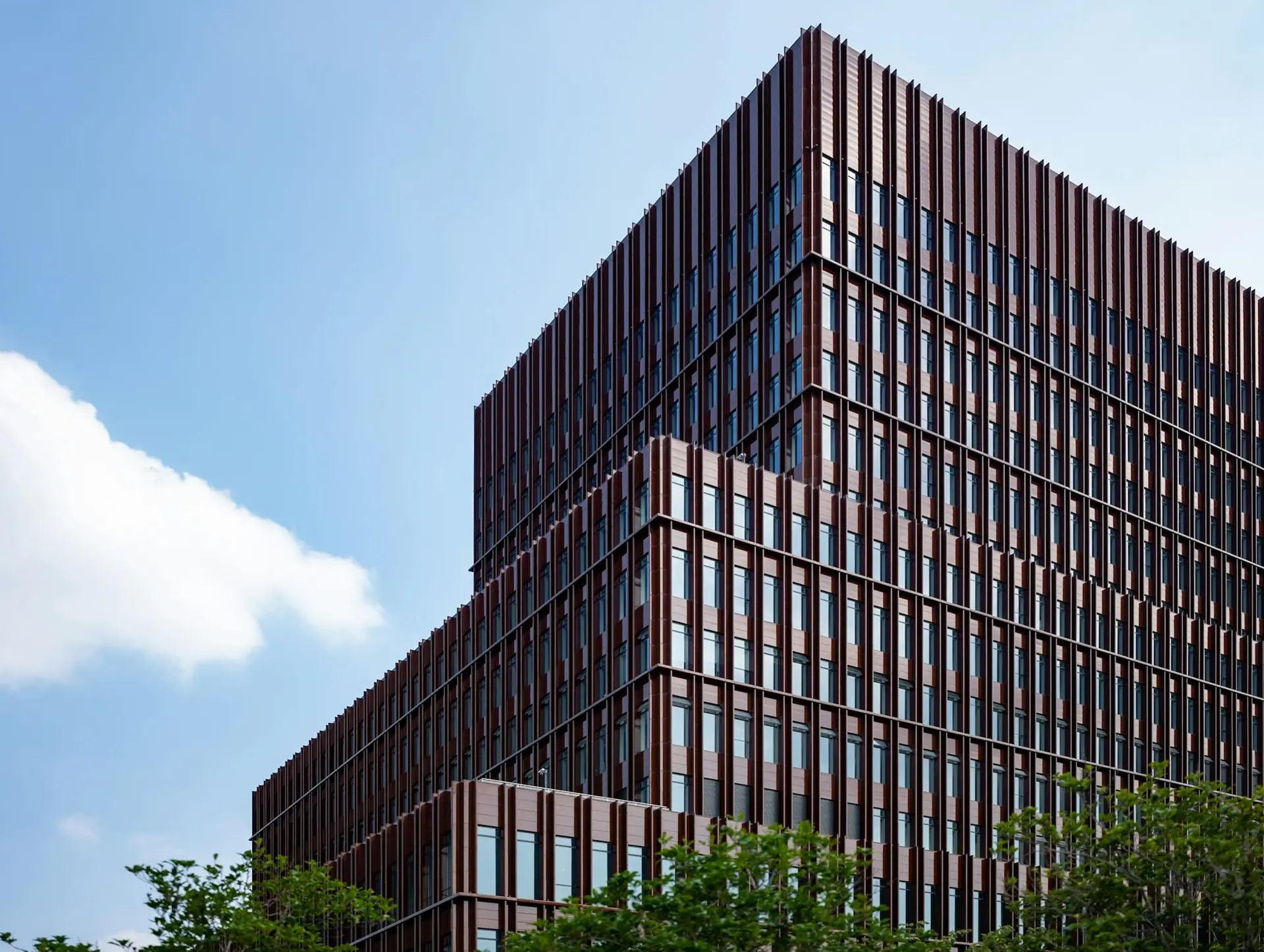 Modern office building with dark red vertical fins and glazing against a blue sky