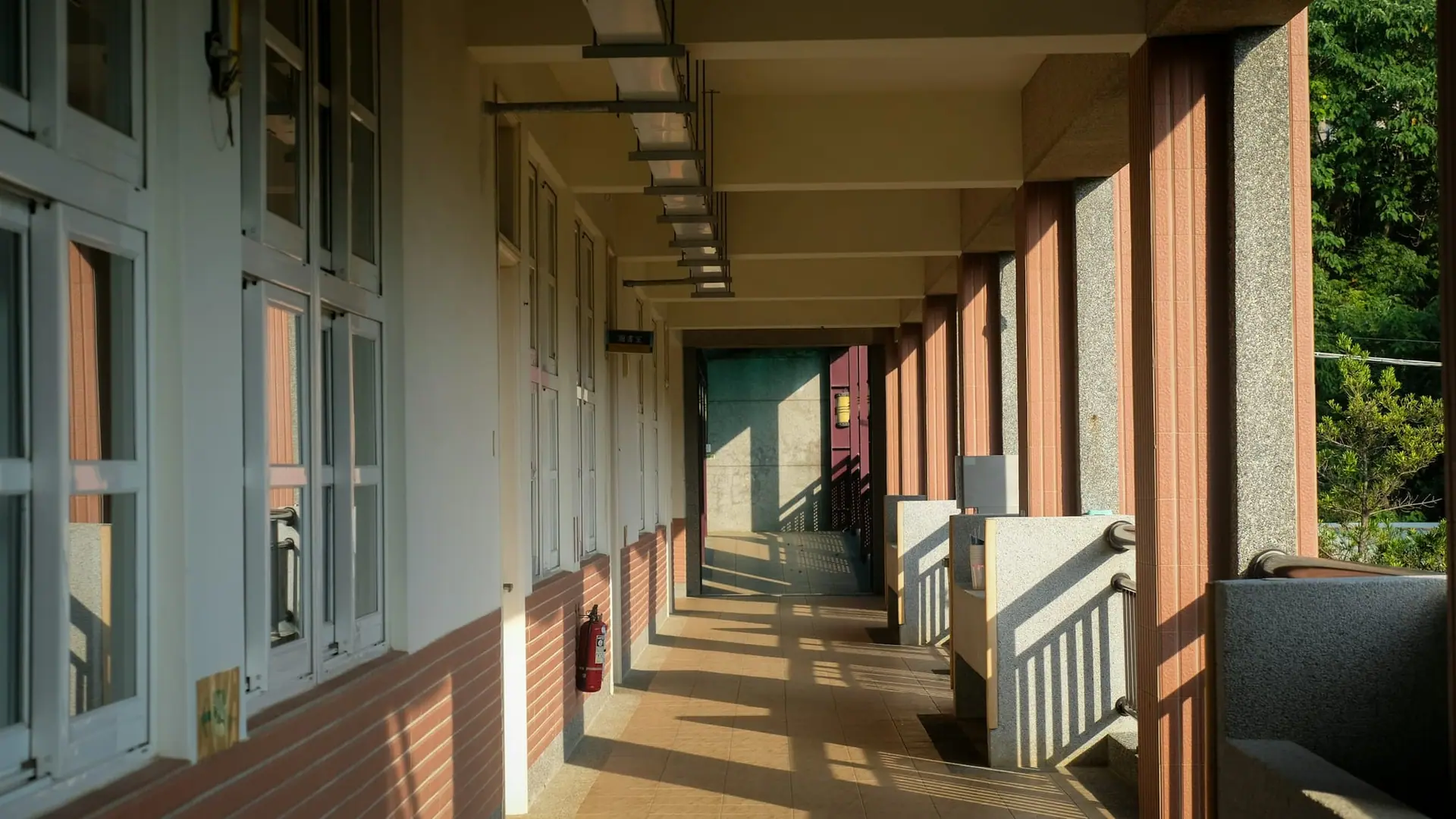 Sunlit open-air school corridor with classroom windows, pillars and tiled floor