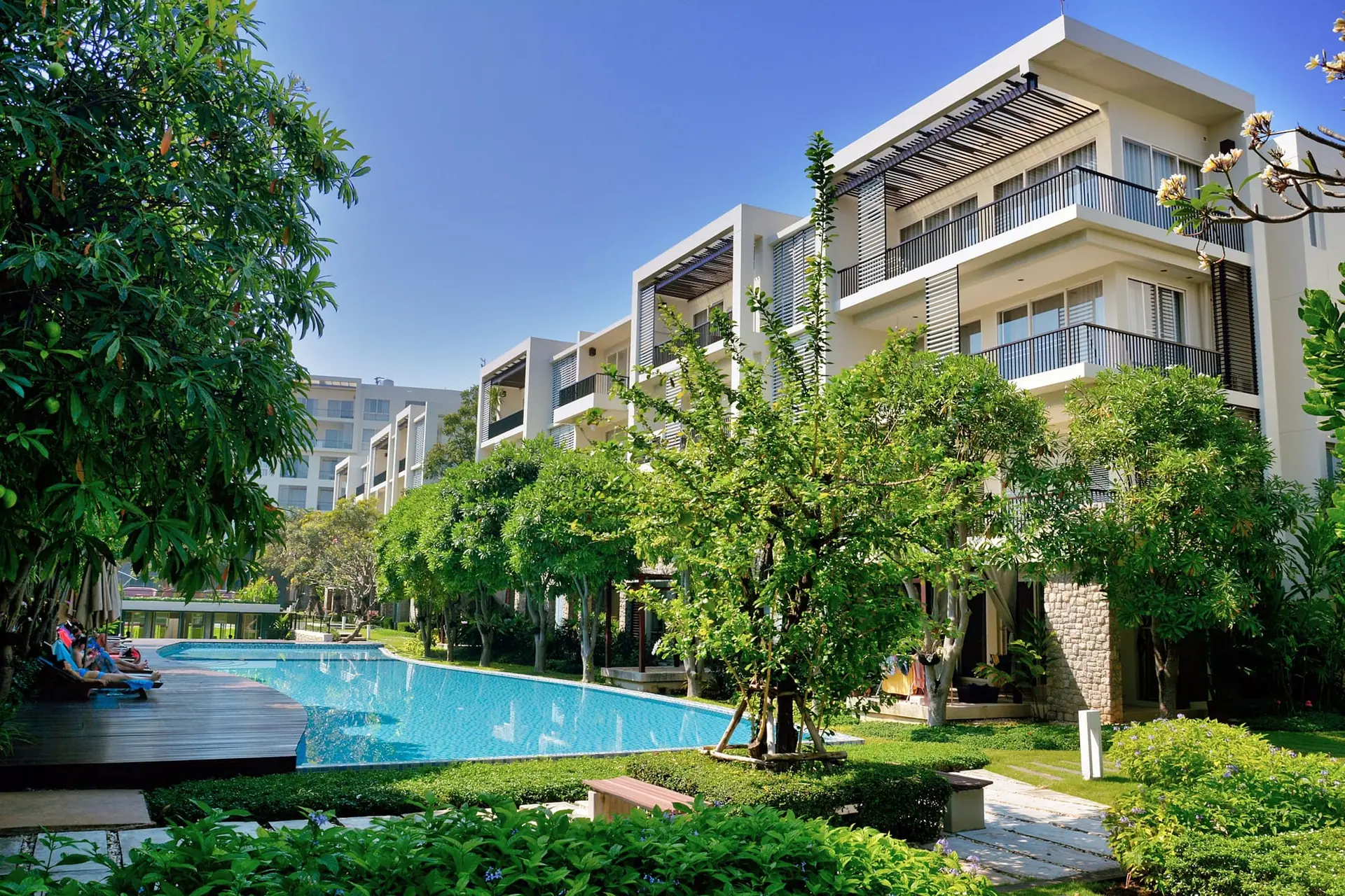 Low-rise condominium buildings with balconies around a swimming pool and tropical garden
