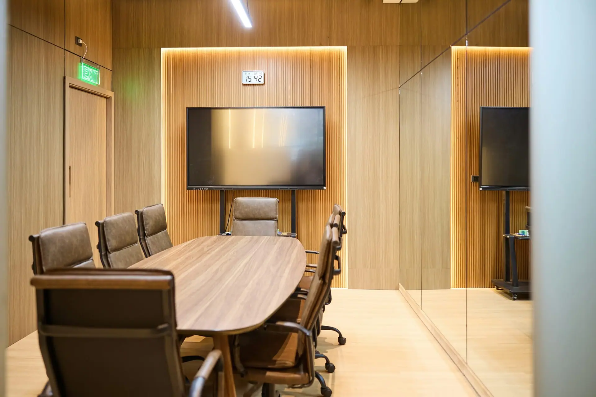 Wood-panelled meeting room with a conference table and a large wall display on a stand